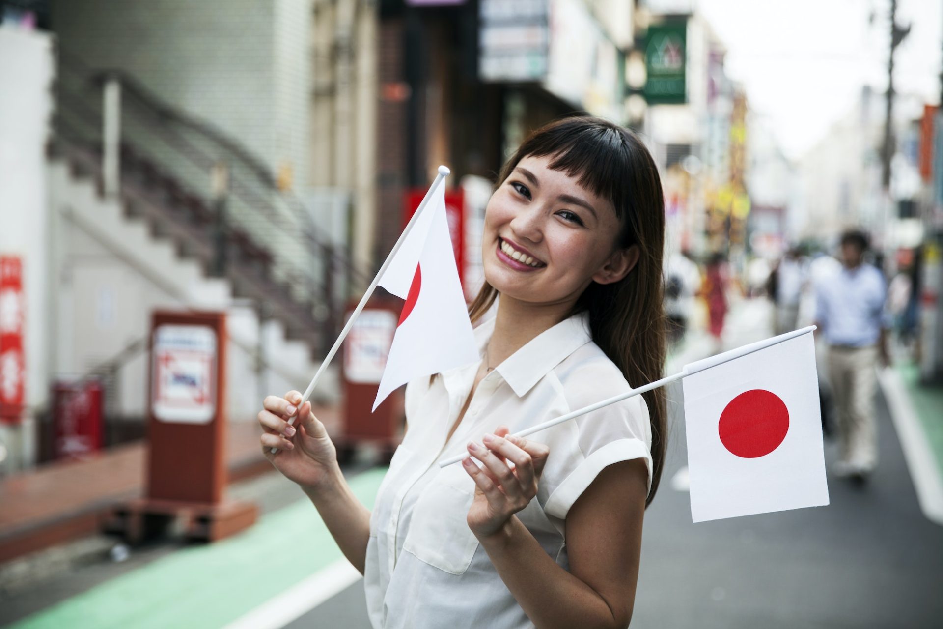 Smiling Japanese woman standing in a street, holding small Japanese flag.