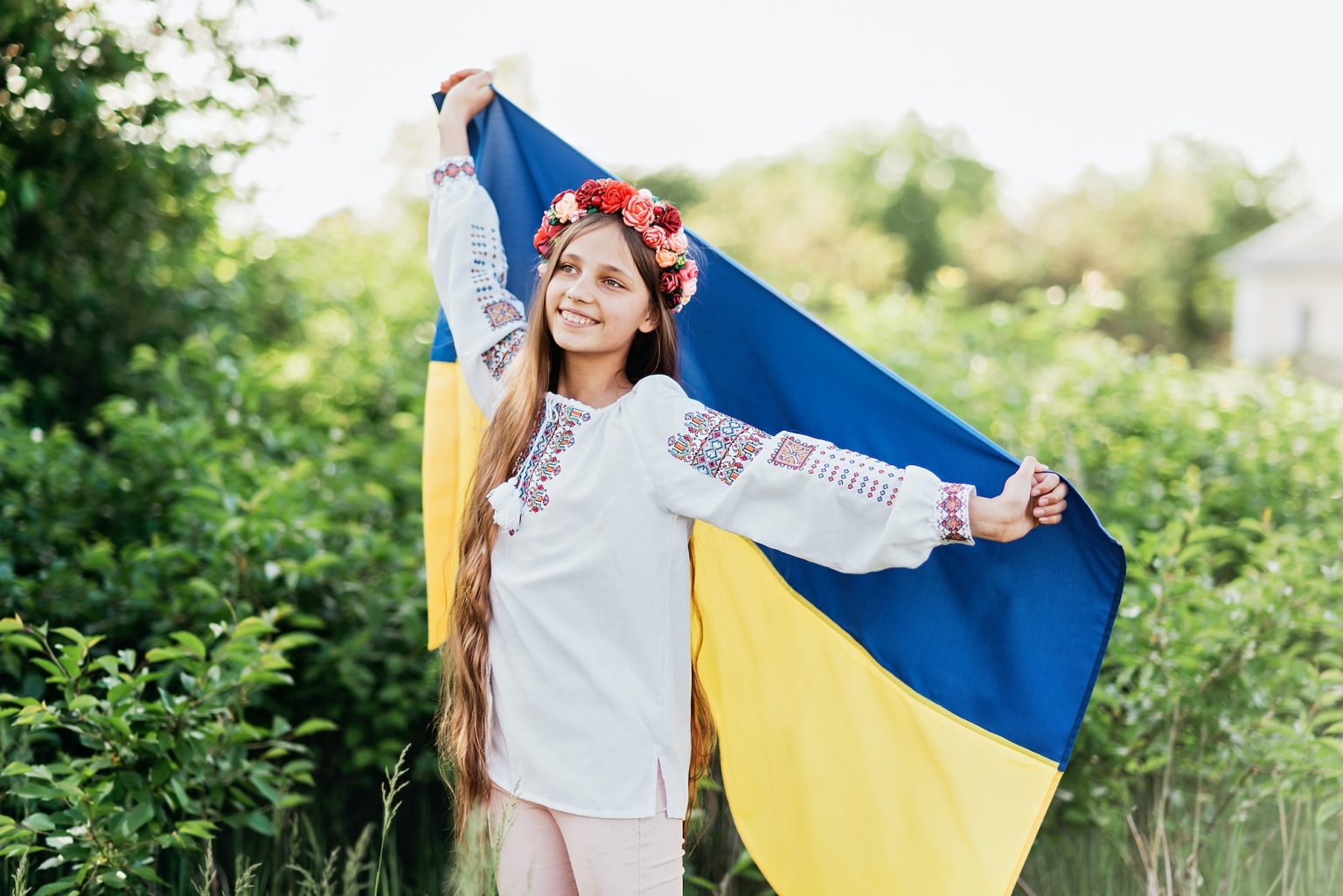 Ukrainian child girl in embroidered shirt vyshyvanka with yellow and blue flag of Ukraine in field.